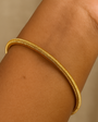Gold bracelet on a wrist against a beige background