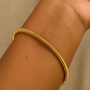 Gold bracelet on a wrist against a beige background