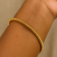 Gold bracelet on a wrist against a beige background
